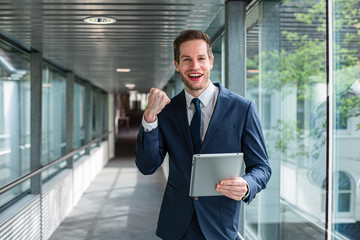 Erfolgreicher, glücklicher Business Mann mit Tablet im Anzug freut sich über seinen Erfolg