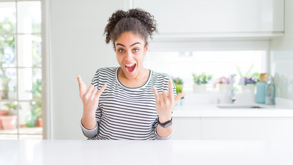 Beautiful african american woman with afro hair wearing casual striped sweater shouting with crazy expression doing rock symbol with hands up. Music star. Heavy music concept.