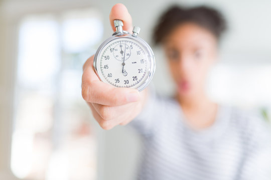 Young african american woman holding stopwatch scared in shock with a surprise face, afraid and excited with fear expression