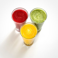 Three colorful fruit smoothies, mango, grape, melon, cabbage, beetroot, lime, on a white background with shadow projection