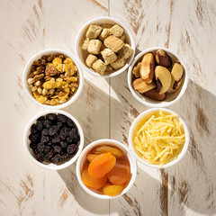 Six ramekins with cereal, croutons, brazil nuts, parmesan cheese, turkish apricot and raisin, on a white wooden table