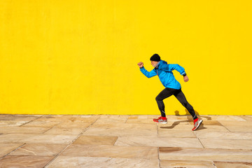 Side view of a senior man running against yellow wall in a bright day