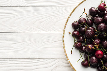 top view of fresh, sweet and ripe cherries covered with droplets on white plate