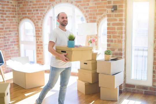 Young handsome man moving to a new house, holding cardboxes smiling very happy for new apartment
