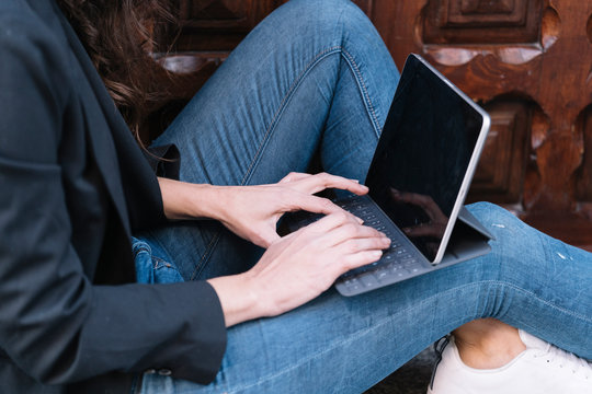 Side view of unrecognizable woman using digital tablet while relaxing on threshold of old wooden door