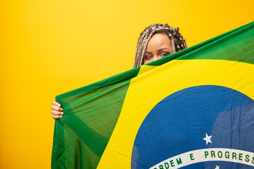 Afro girl cheering for favorite brazilian team, holding national flag in yellow background.