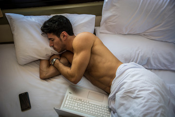 Close Up of Young Man with Dark Hair Sleeping on Bed Next to Laptop Computer and Cell Phone, Tired from Too Much Work