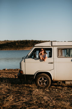 Pretty young brunette smiling and looking away while sitting inside vintage car on blurred background of nature