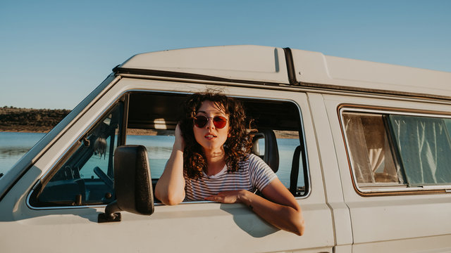 Pretty young brunette smiling and looking away while sitting inside vintage car on blurred background of nature