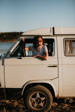 Pretty young brunette smiling and looking away while sitting inside vintage car on blurred background of nature