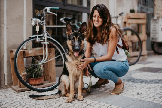Cute german shepherd standing close bicycle on cobblestone pavement with owner cuddling