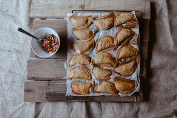 Baking tray with composed freshly baked pies patty having golden crispy crust near bowl with peeper and onion