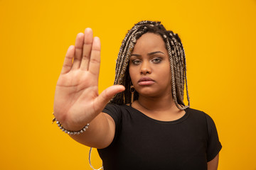 Fototapeta premium Young African American woman shown hand on sign for them to stop with racial prejudice.