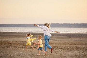 Happy family of mother and two children  launch a kite on nature at sunset. They having fun and running. Straightened their arms like a plane