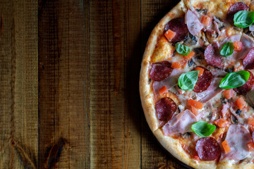 Appetizing pizza with mushrooms, salami, pepper, ham, tomatoes, Basil and mozzarella on a beautiful wooden background