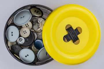 gelbe Knopfdose gefüllt mit verschiedenen Knöpfen
