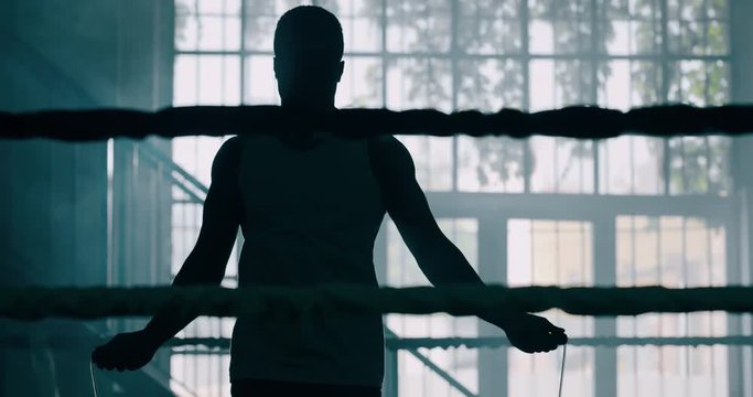 Cinematic slow motion shot of a professional young muscular african man is jumping rope before shadow boxing work out in a ring. 