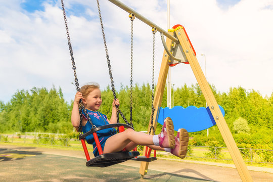 Happy Little Child Girl Laughing And Swinging On A Swing In The City Park In Summer