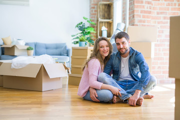 Fototapeta na wymiar Young beautiful couple in love sitting on the floor together with cardboard boxes around for moving to a new house