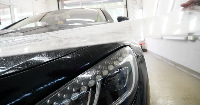 Close up to PPF installation process on a front headlight and hood. PPF is a Paint Protection Film which protect paint from scratches and stone chips. Concept of: Guard, Protect, Car, New, Work.