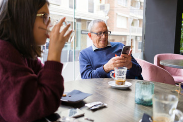 Senior man having a conversation with woman drinking coffee using smartphone and relaxing, chatting at restaurant