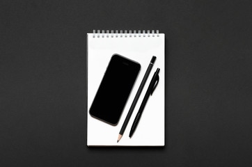 White open notebook with black pencil, pen and smartphone on black background. Office desk, stationery. Top view, flat lay.