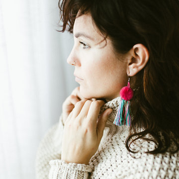 Side view of attractive dreamy young brunette with bright handmade earring of colorful threads