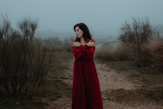 Dreamy woman in red dress walking along empty road of hazed mysterious terrain