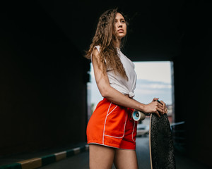 Beautiful skater woman wearing red shorts riding on her longboard in the sunset city