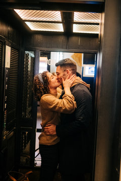 Side view of cheerful young man and woman holding door of elevator and smiling during romantic date