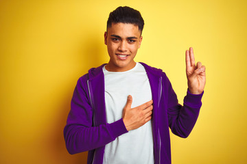 Young brazilian man wearing purple sweatshirt standing over isolated yellow background smiling...