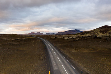 Aerial above view of empty icelandic road leading to sunset and mountains