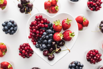 top view of whole cranberries, strawberries, blueberries and cherries on heart shaped plate