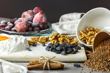 Baking ingredients on gray background. Randomly scattered foods, frozen fruits, nuts, cinnamon, flax seeds, flour, eggs. 