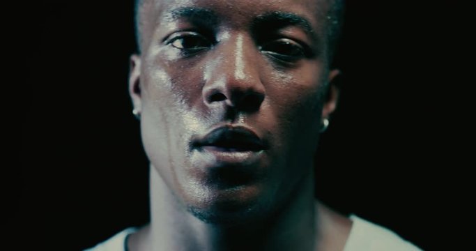Cinematic slow motion shot of a professional young sweaty african man is looking in camera after practicing shadow boxing work out in a ring. 