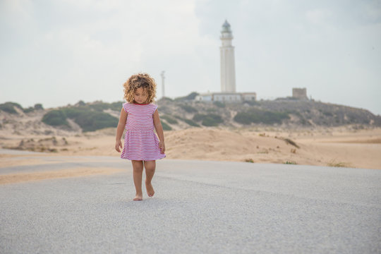 curly child in striped walking on road of sand beach on blurred nature background