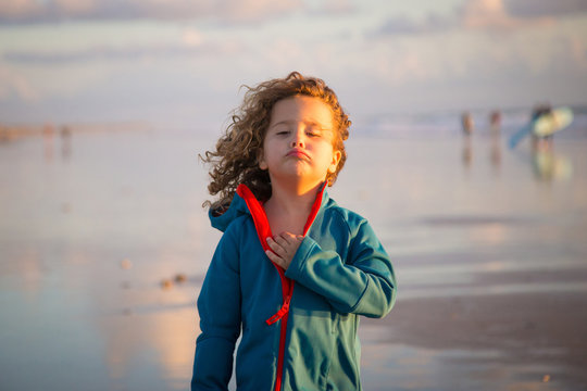 curly child in striped walking on beach on blurred nature background