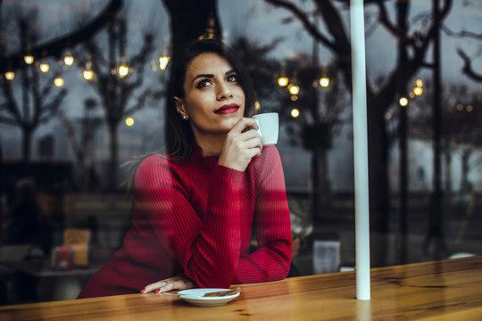 Young woman with cup of coffee behind windowpane in a cafe