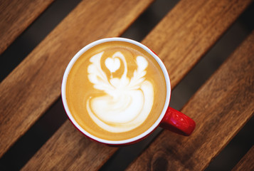 Cup of coffee with latte art on wooden table in cafe.
