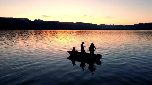 Silhouette of fishermen during sunset on a boat as one jigs fishing pole trying to catch a fish at Hebgen Lake.