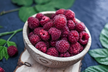 Fresh red ripe raspberries in a wooden cup on a dark background. Near green leaves. Red berries on a dark background.