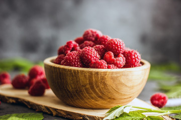Fresh raspberry berries in a wooden bowl on a table against a dark background. Near the fresh raspberry leaves. Copy space, look straight. Background with fresh summer red berries.