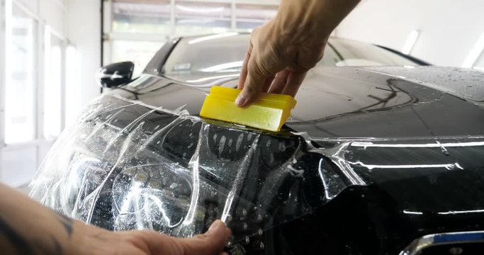 Close up to PPF installation process on a front headlight and hood. PPF is a Paint Protection Film which protect paint from scratches and stone chips. Concept of: Guard, Protect, Car, New, Work.