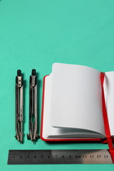 Accessories for drawing. Compasses, ruler and notebook. Against the background of mint color.