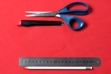 Accessories for application. Scissors, knife, pencil and ruler. Against the background of coral color.