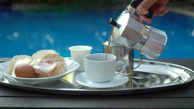 Man pours a coffee into the cup on the background of the pool