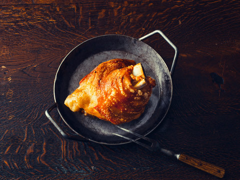 Crispy roasted pork knuckle in a pan on wooden table
