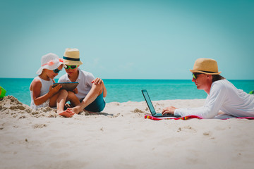 father working on laptop while kids looking at touch pad at beach