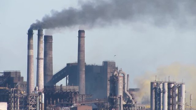 Air pollutants emissions - colored smoke. Orange and black smoke of air pollutants, released into the atmosphere by chimney smoking stack, pollutes the environment, causing the global warming.
