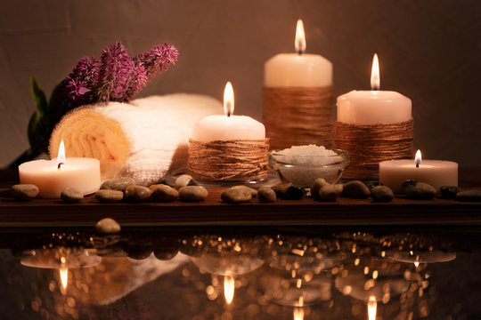 Spa decorative set with sea pebbles, salt, aromatic candles, towel and flower. Golden composition in low key, dark photo with beautiful reflections and bokeh.